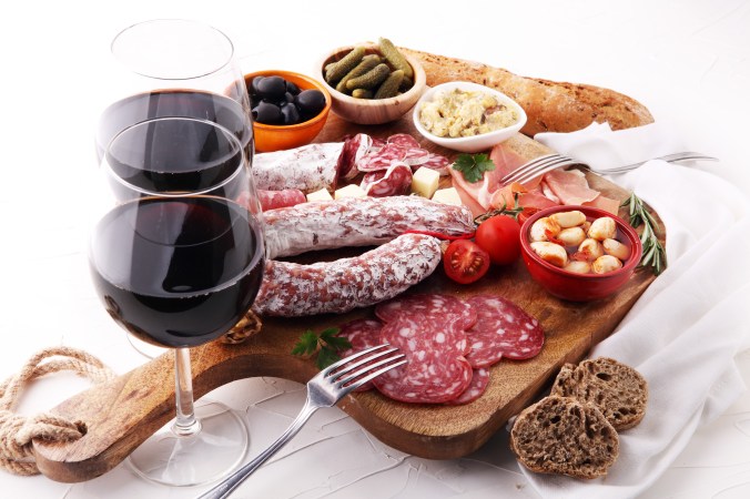 Italian antipasti wine snacks variety set. Cheese, Mediterranean olives, pickles, Prosciutto di Parma, tomatoes, artichokes and wine in glasses. Spanish tapas